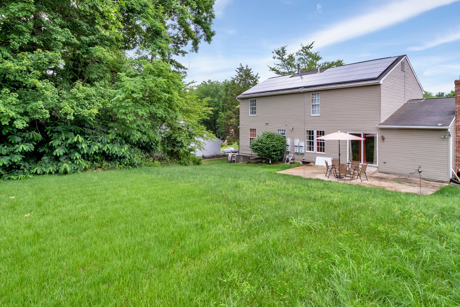 The backyard of a house with a large lawn and patio area.