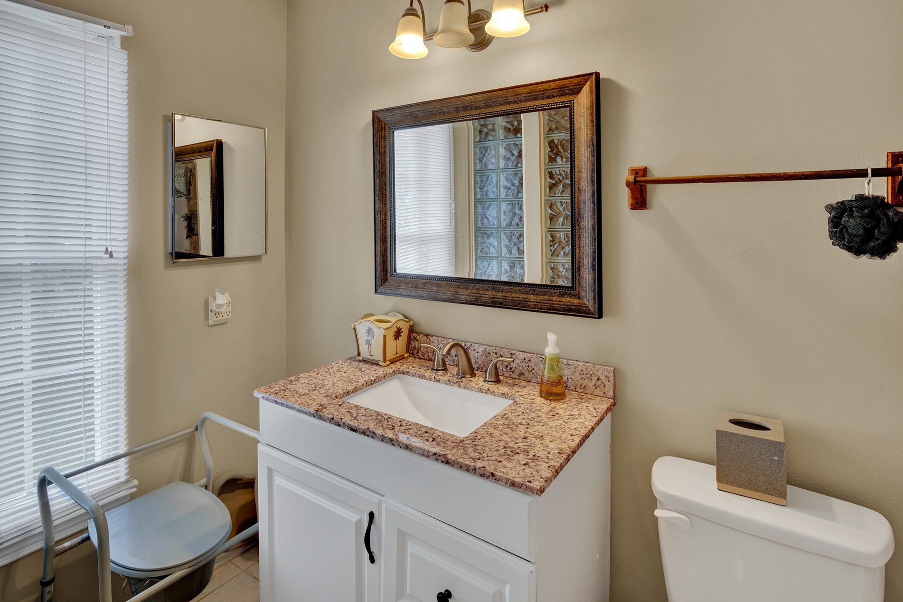 A bathroom with a sink , toilet , mirror and window.