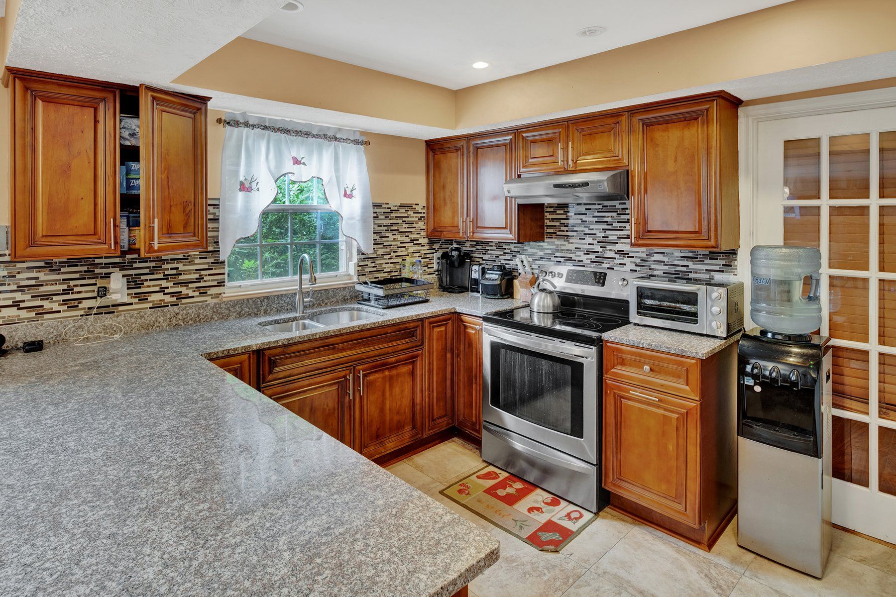 A kitchen with wooden cabinets , granite counter tops , stainless steel appliances and a water dispenser.