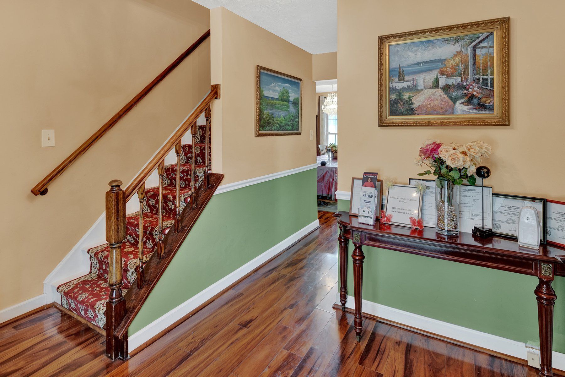 A hallway with stairs , a table and a painting on the wall.