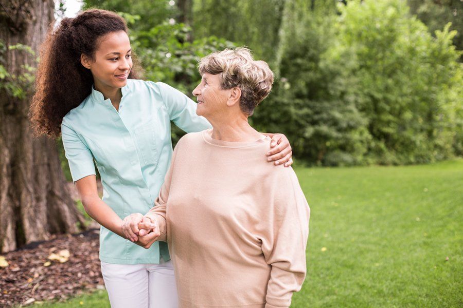 A nurse is holding the hand of an elderly woman in a park.