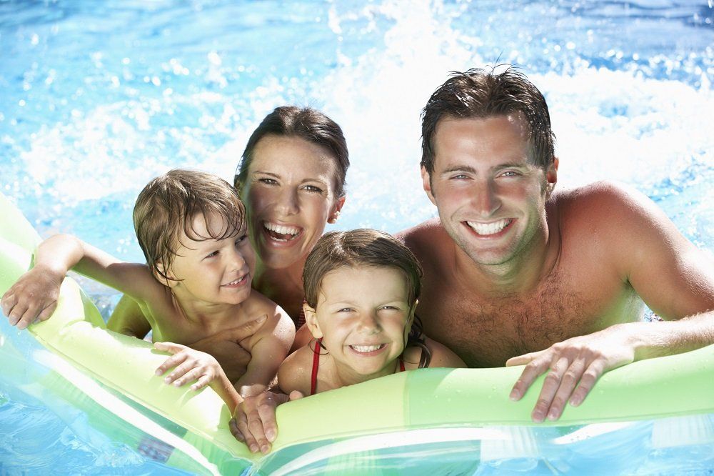 Smiling family in a green inflatable pool, splashing in bright blue water