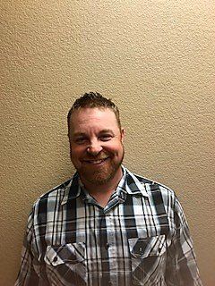 Smiling man in a plaid shirt standing against a beige wall