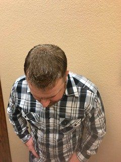 Man in plaid shirt seen from above, standing against a beige wall and looking down