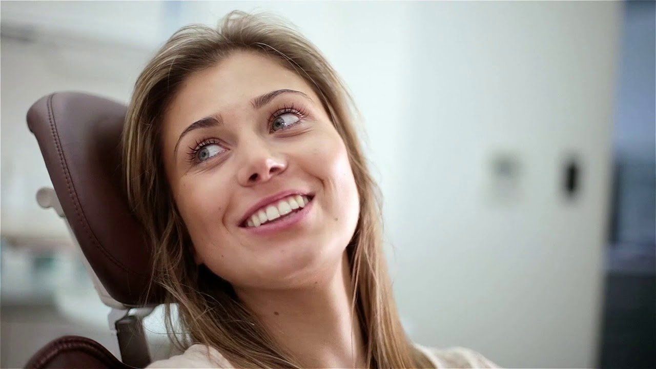Woman smiling in a dentist's chair, looking up, with a bright smile.