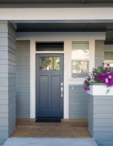 Gray front door with sidelights on a modern porch, with a purple flower basket nearby