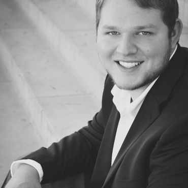 Smiling man in a dark suit seated against a light stone wall