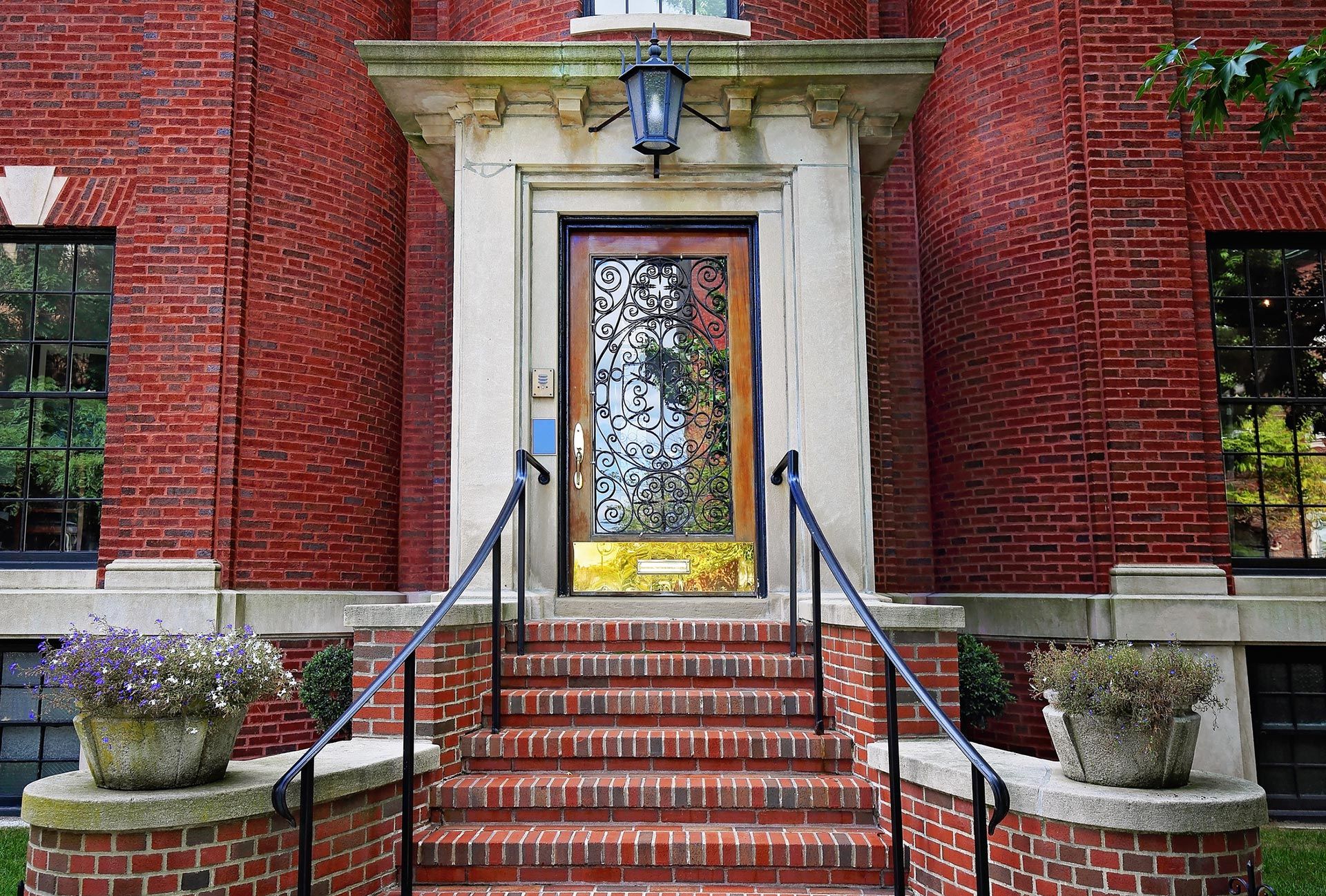 Brick building entrance with white stone doorway, blue lamp, and stairs with black railings