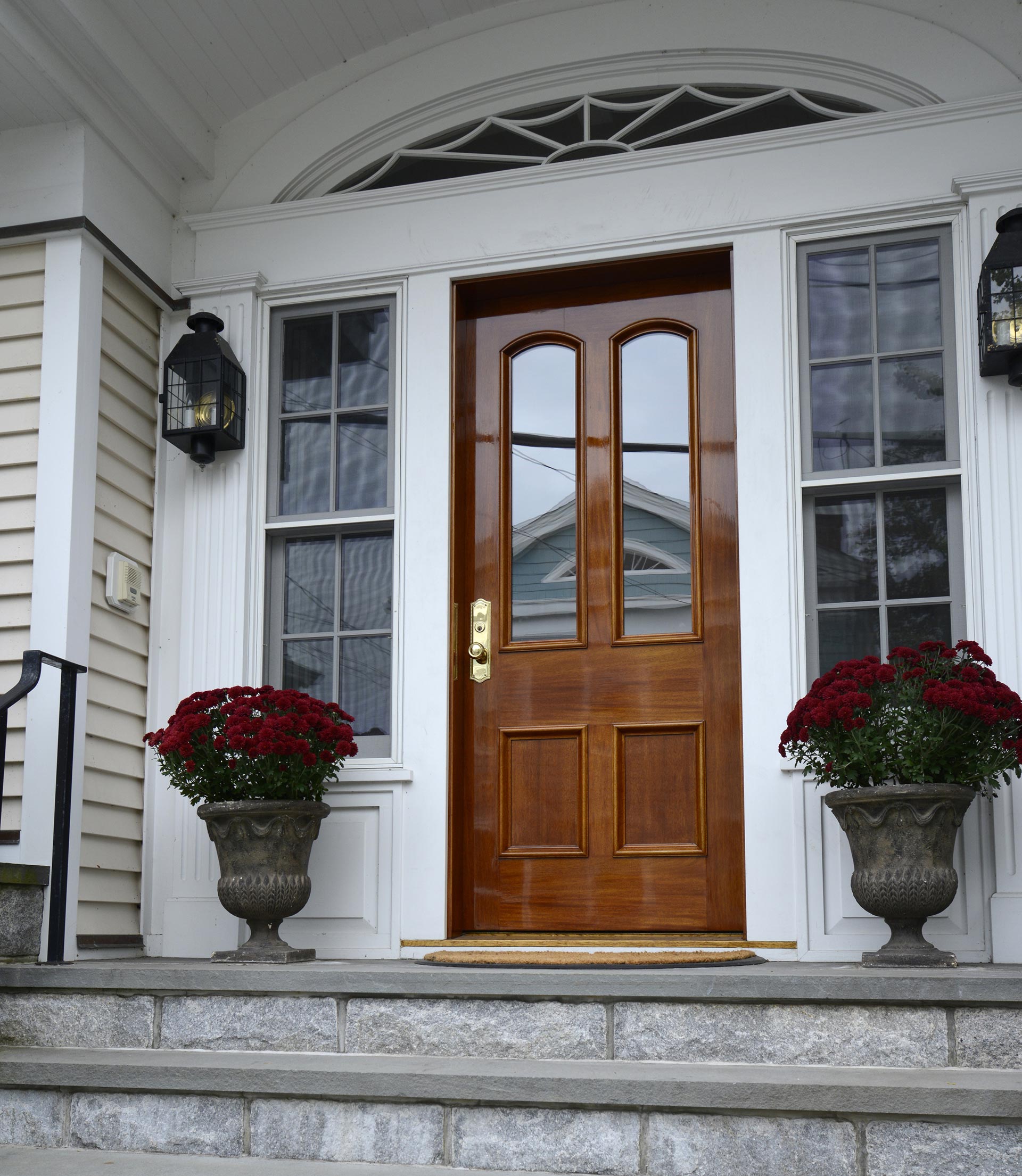 Front porch with a wooden double door, white trim, stone steps, and potted red flowers on either side.