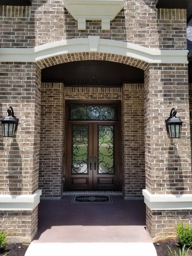 Brick house front entrance with arched porch, double wooden doors, and wall lanterns