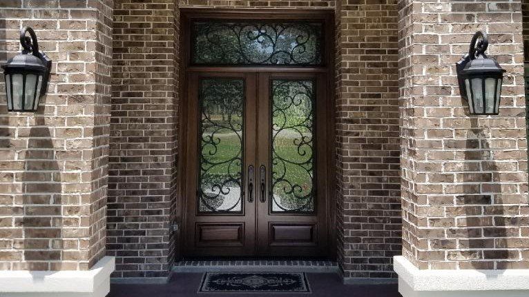 Brick house entrance with double wooden doors, decorative glass, and wall lanterns