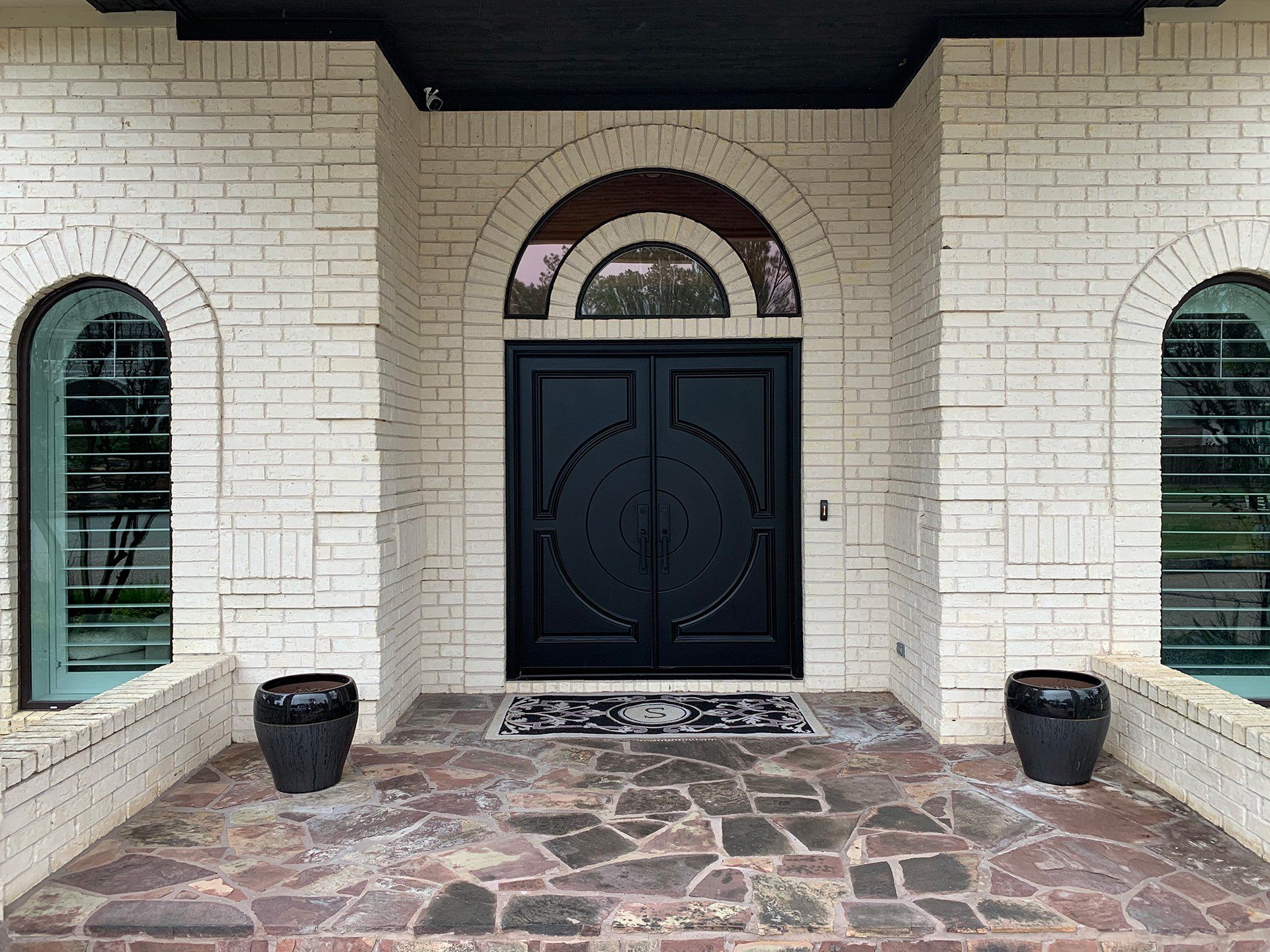 Front entrance with black double doors, white brick walls, arched windows, and stone walkway