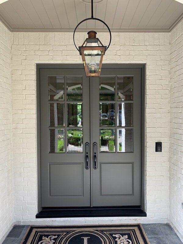 Gray double front doors with glass panes, a hanging lantern, and white brick entryway.