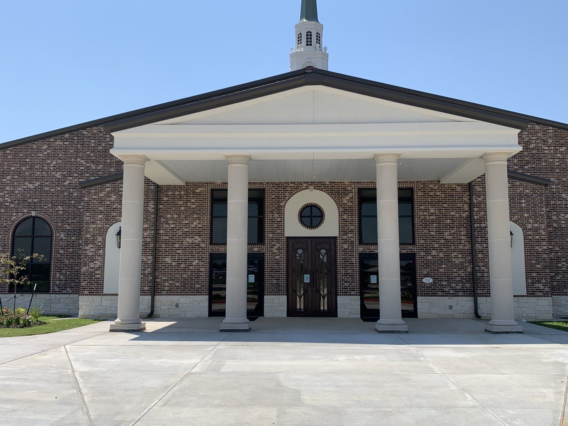 Brick church entrance with white columns, arched doorway, and a small steeple above.