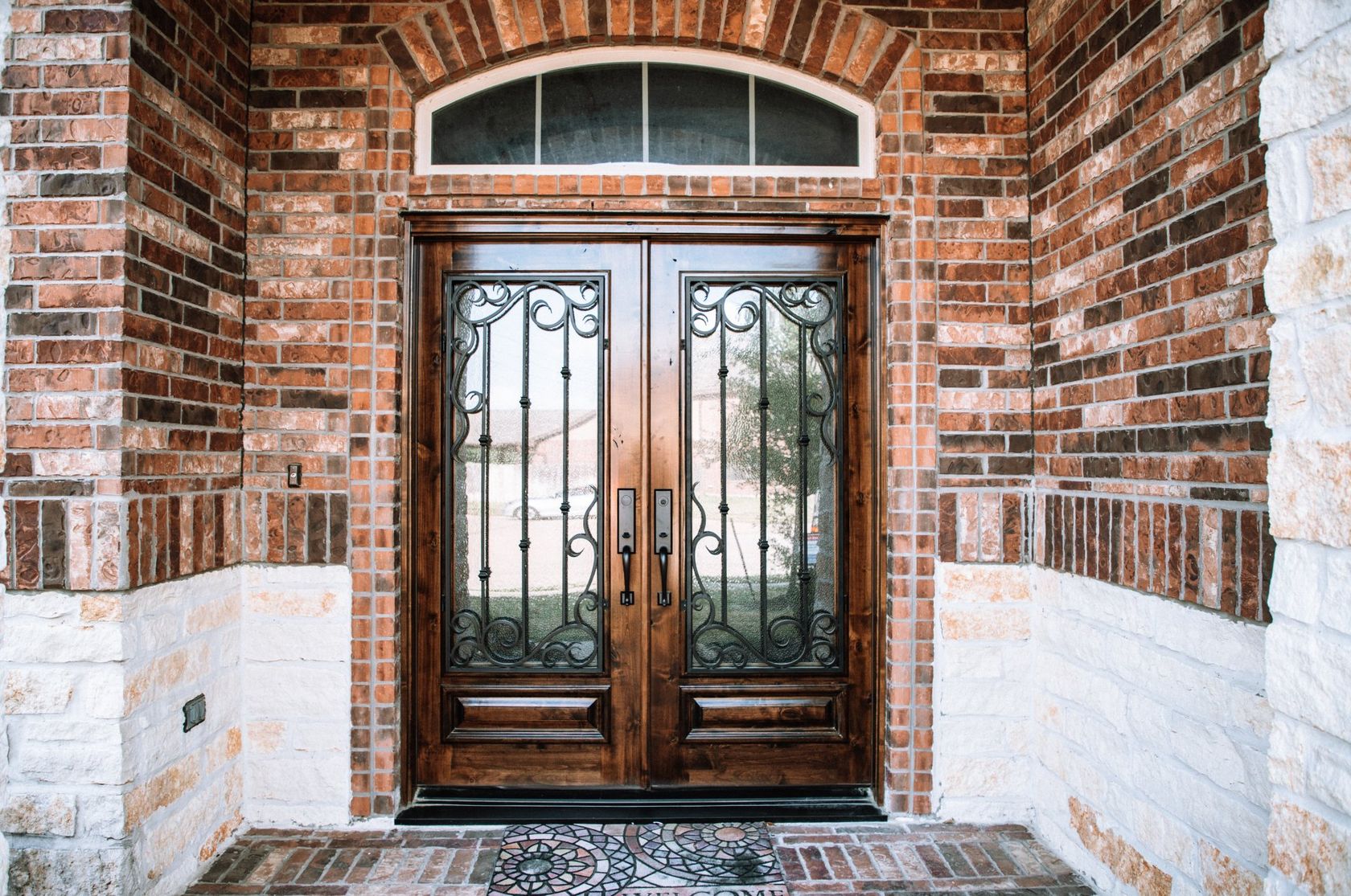 Brick entryway with double wooden doors and arched transom window