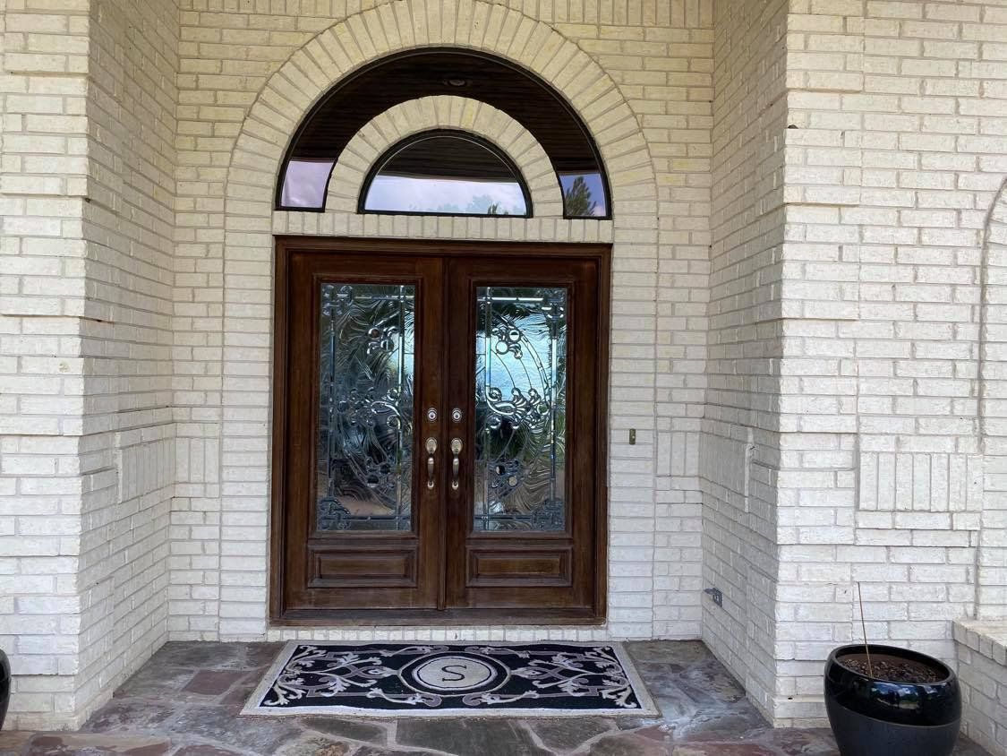 Front entrance with dark wood double doors, arched transom, and patterned rug under a brick archway