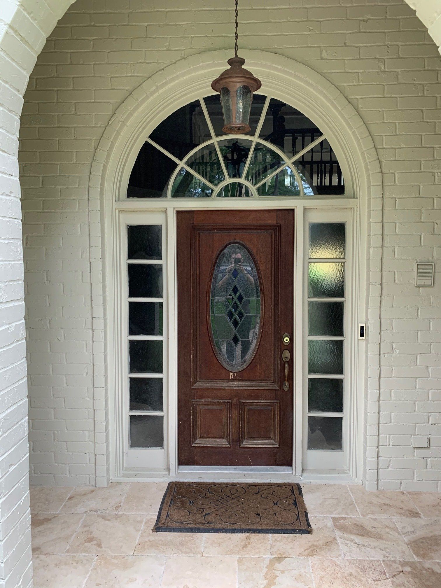Front entrance with arched wooden door, sidelights, and hanging lantern under a brick archway