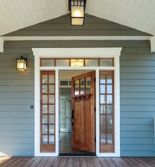 Open wooden front door with glass panels on a gray house porch under a hanging light