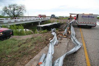 Tractor-trailer requiring major truck wrecker service beneath damaged guardrail