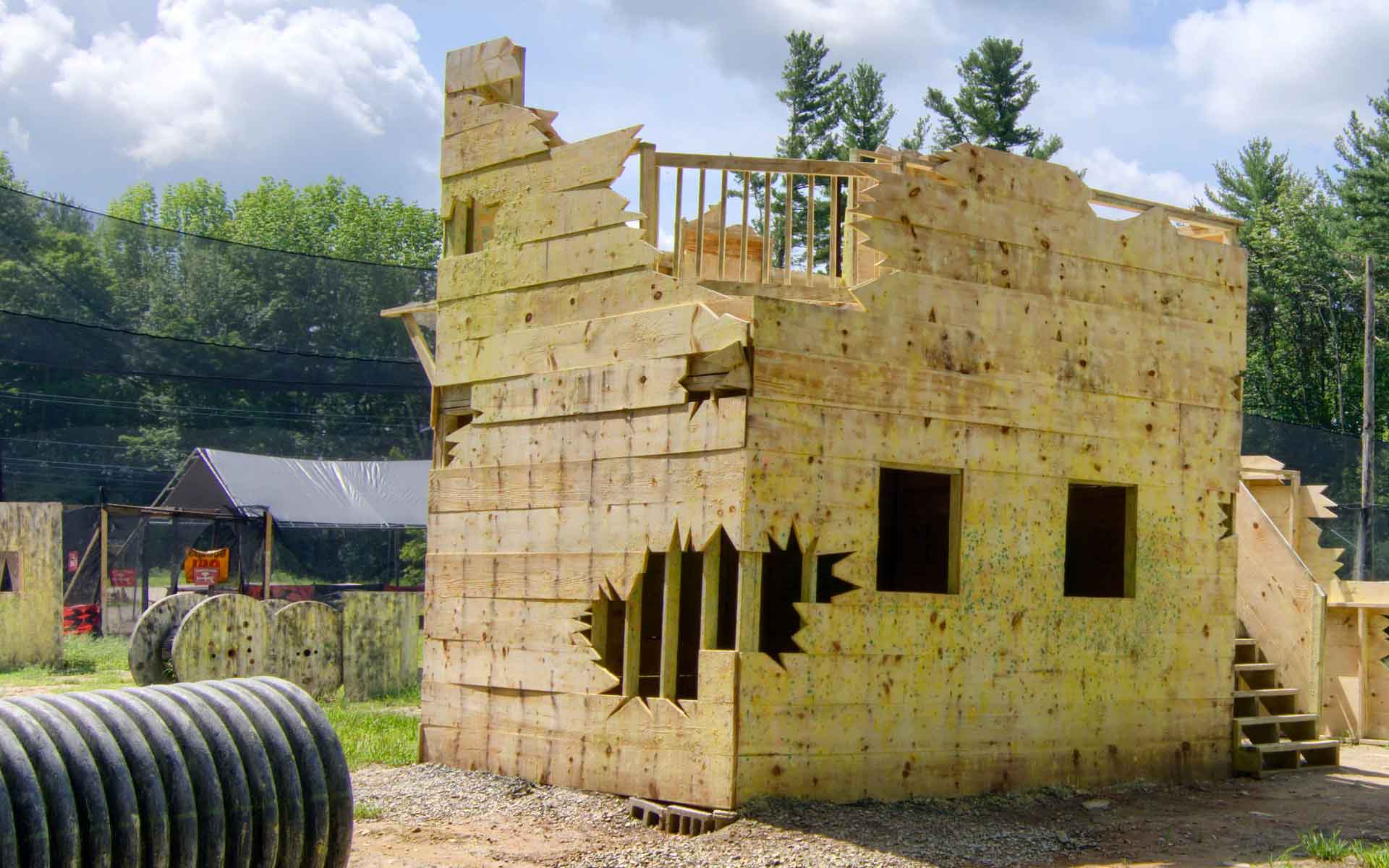 A two-story paintball building with many paint marks. Outdoor paintball course with trees in background.