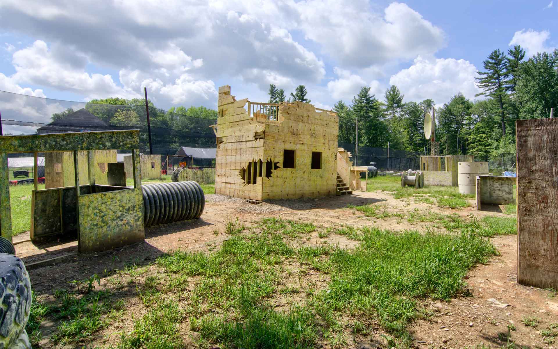 Paintball course with wooden structures and bunkers, set in a grassy field, under a sunny sky.