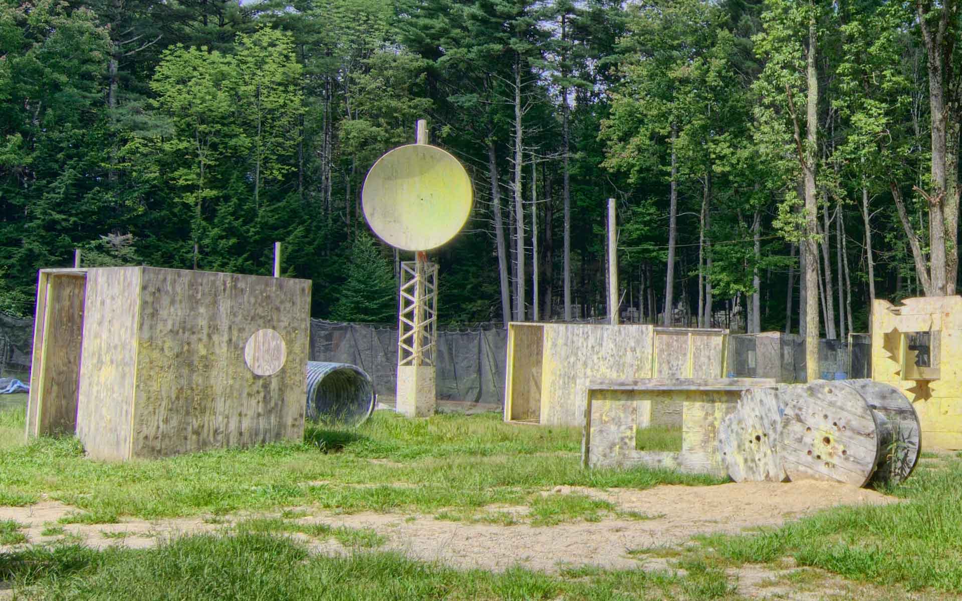 Paintball field with concrete bunkers, large target, and trees in the background.