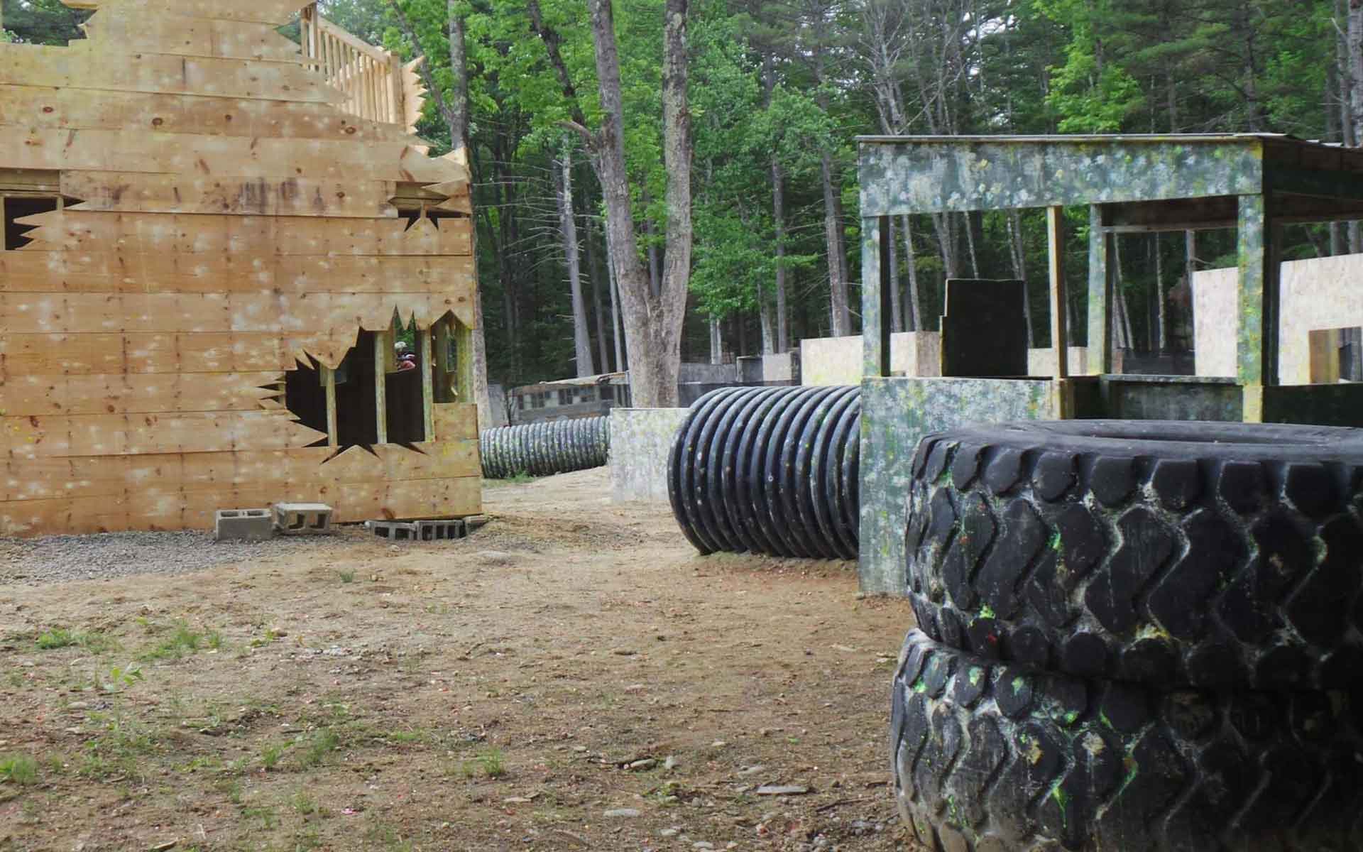 Paintball field with wooden structures, tires, and a tunnel in a wooded area.