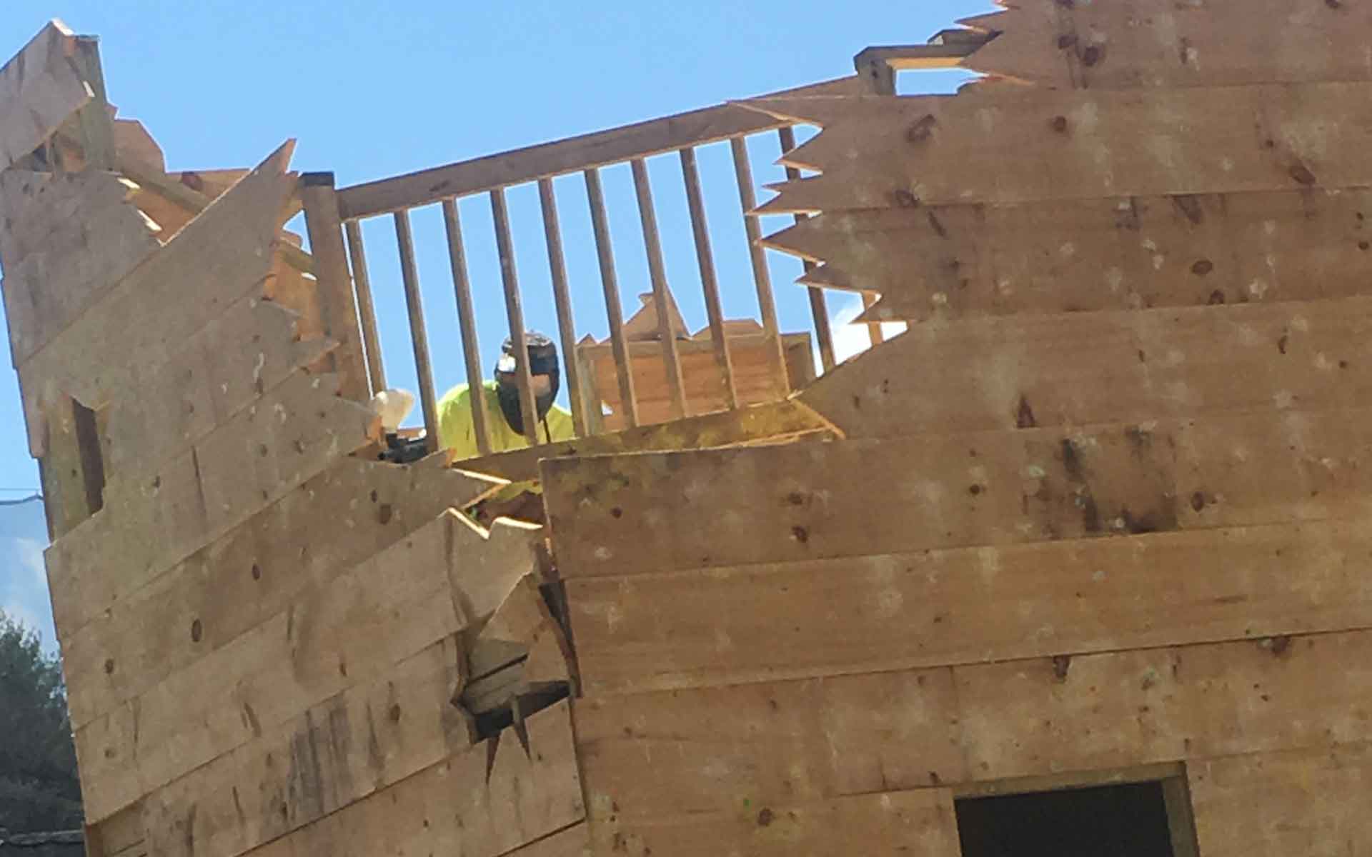 Person in yellow vest and mask looking out from a wooden structure with a railing, on a sunny day.