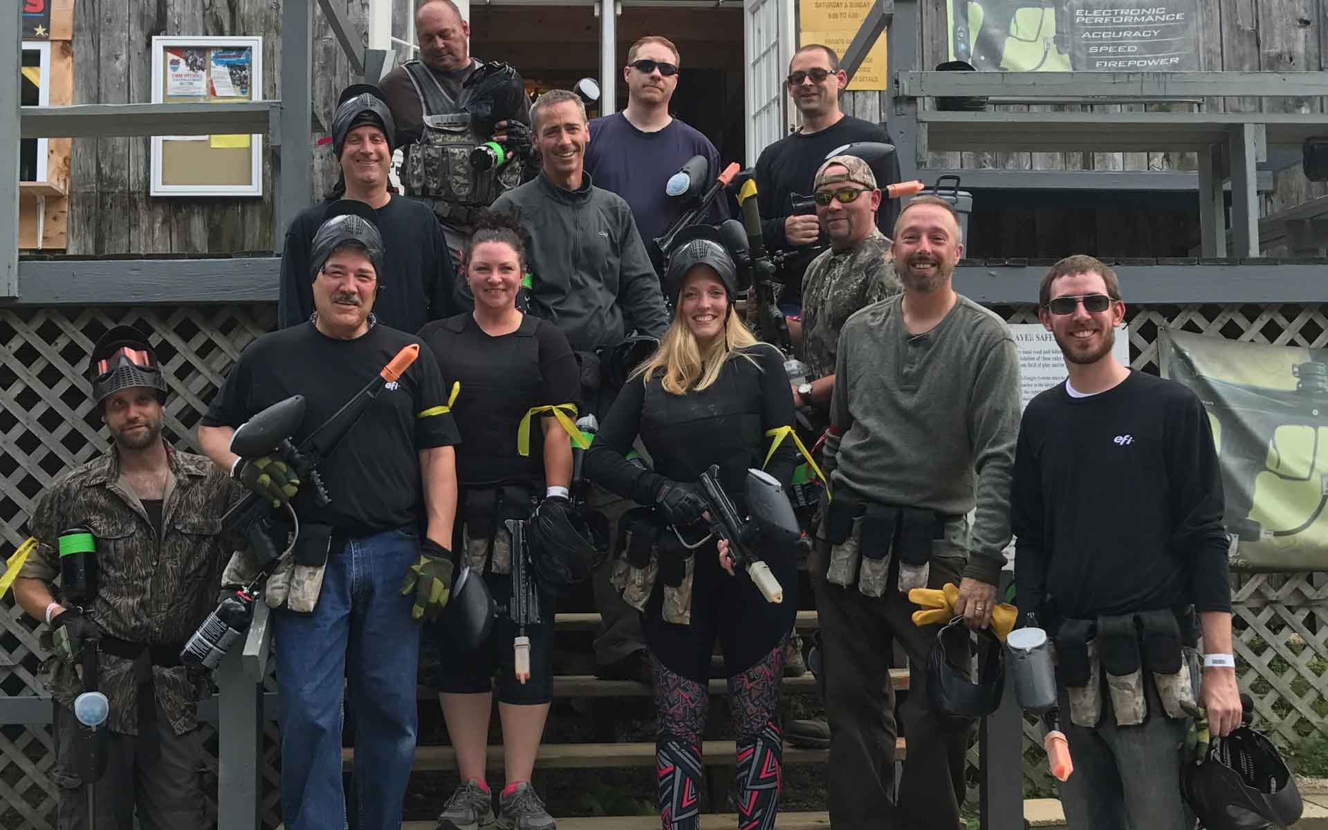 Group of people in paintball gear posing on steps outdoors.