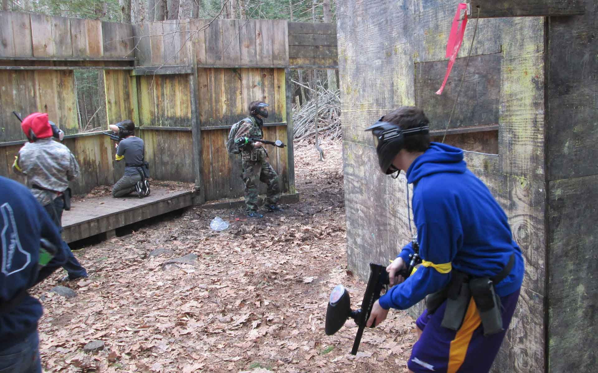 People playing paintball in a wooded area. Players wear protective gear, hold paintball guns