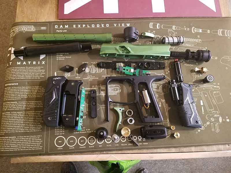 Disassembled paintball gun with green and black parts, on a green mat.