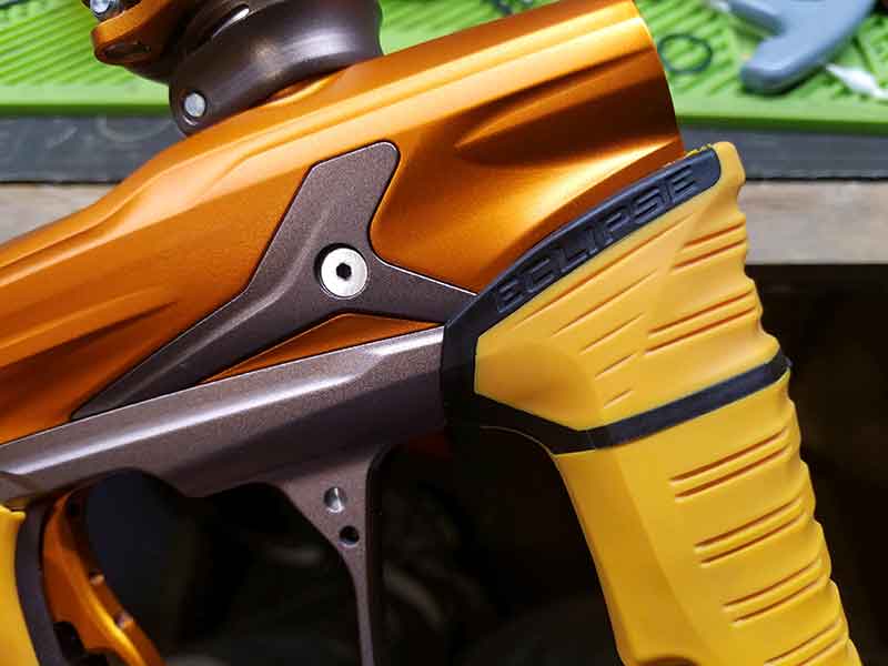Close-up of an orange and yellow paintball gun with dark grey accents.