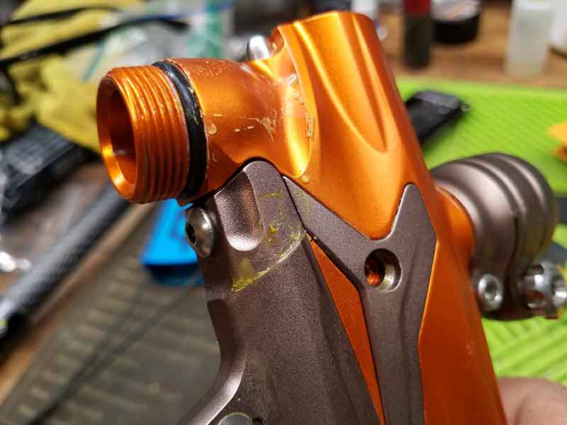 Orange and brown paintball gun with wear marks and a threaded barrel fitting.