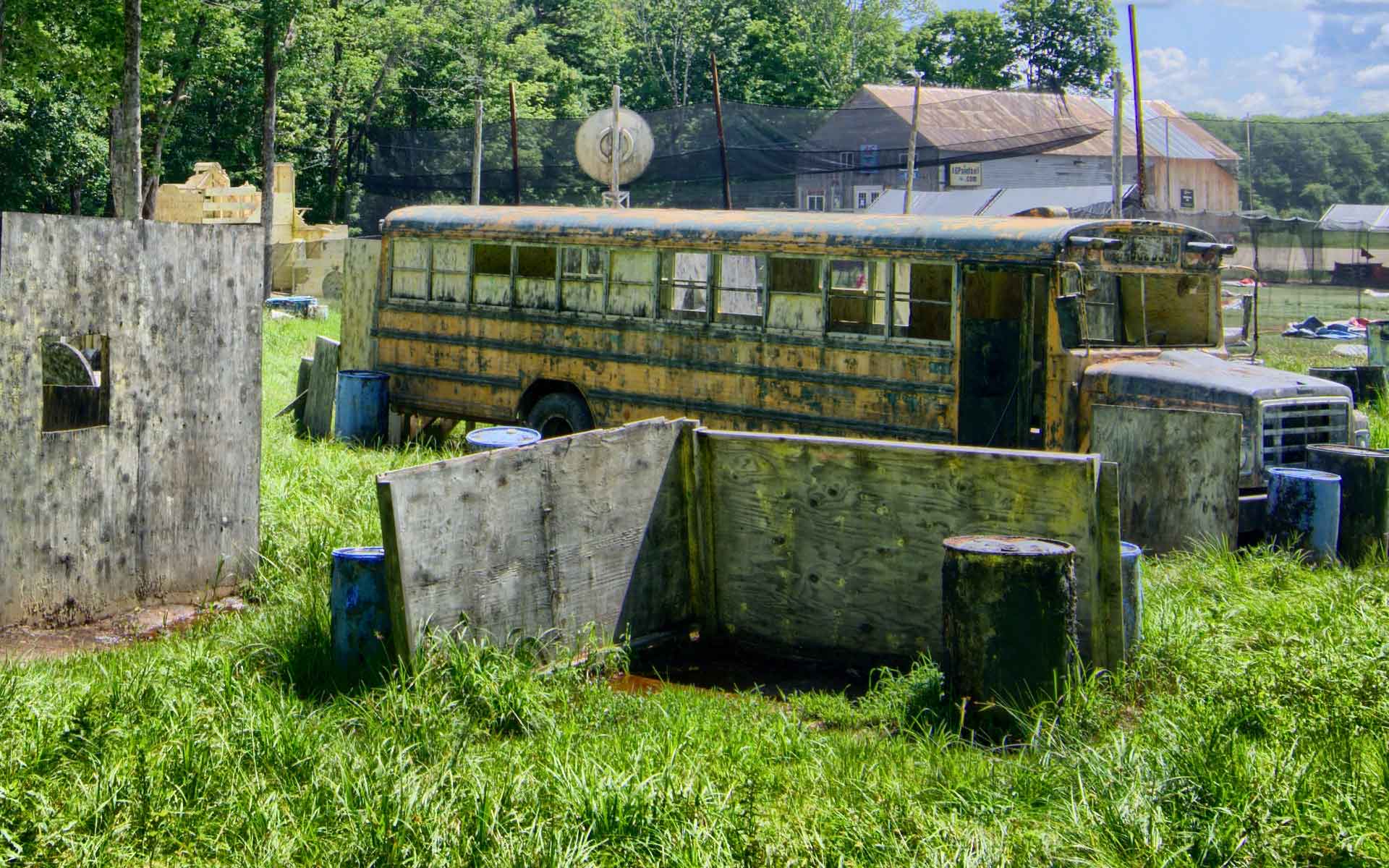 Paintball field with a yellow school bus, concrete barriers, and green grass.