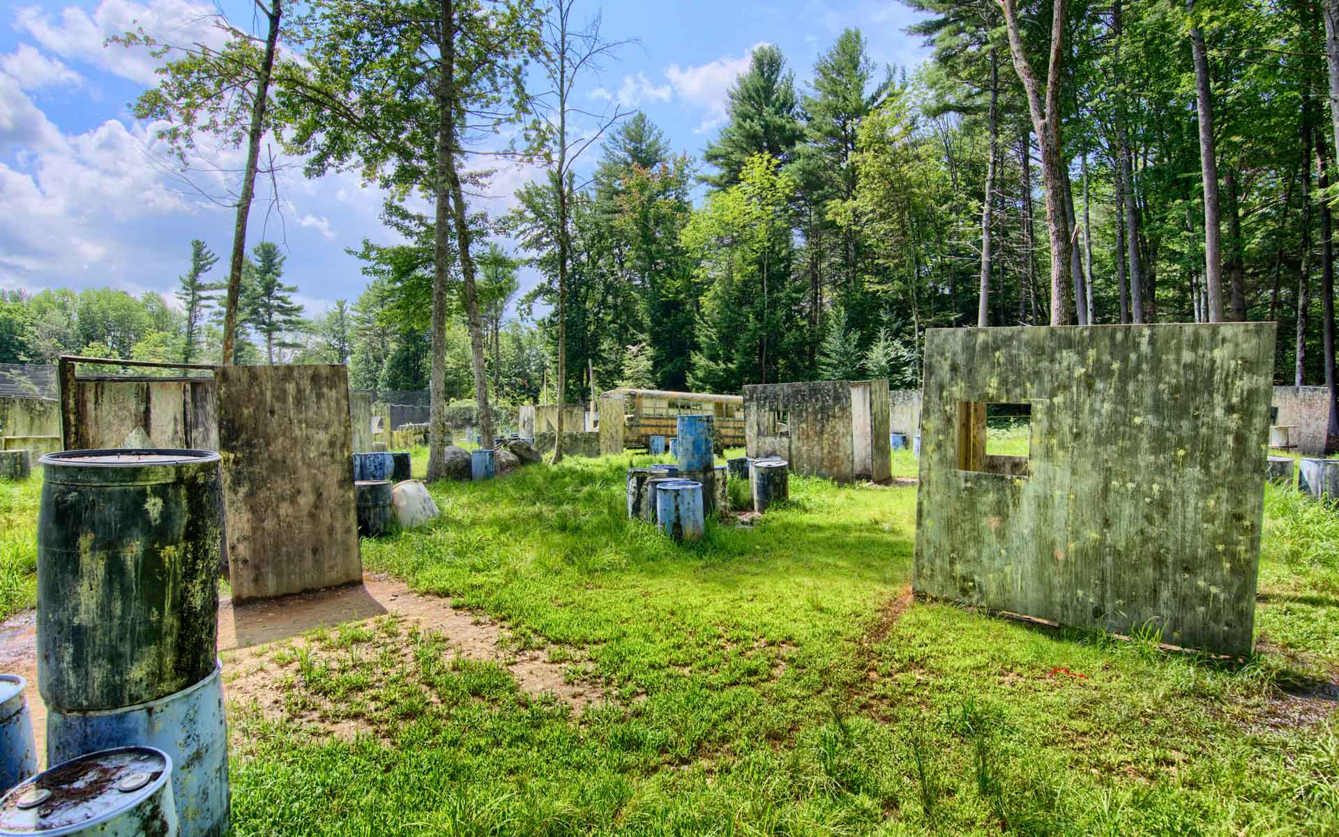 Paintball field with concrete barriers, lush green grass, and trees under a bright sky.