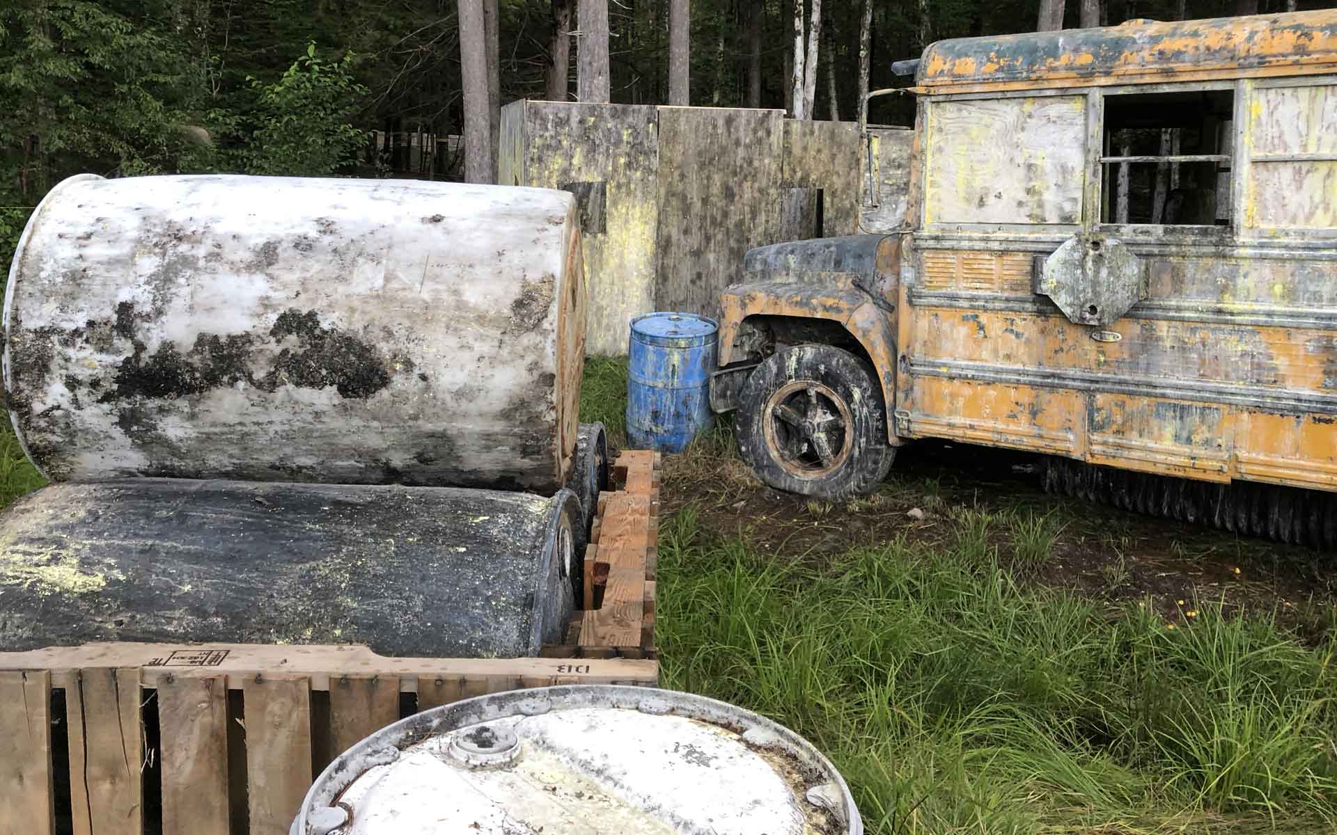 Paintball course with a yellow school bus, barrels, and wooden barriers.