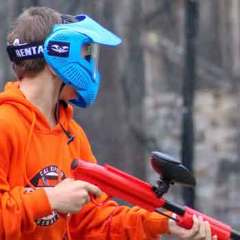 Person in orange hoodie and blue paintball mask holding a red paintball gun.