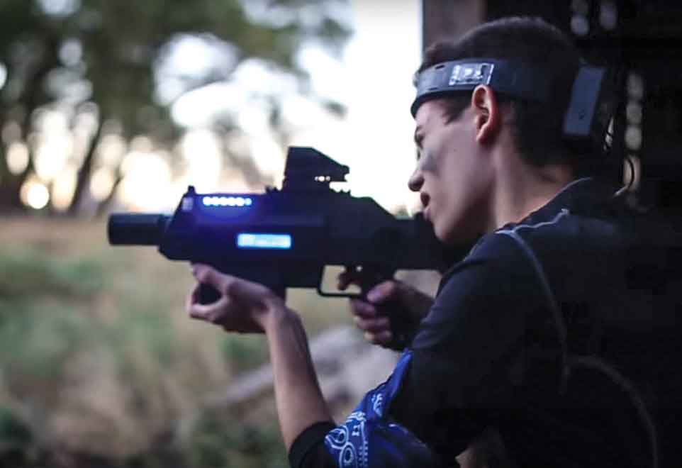 Person aiming a laser tag gun. Dark setting, trees in background.
