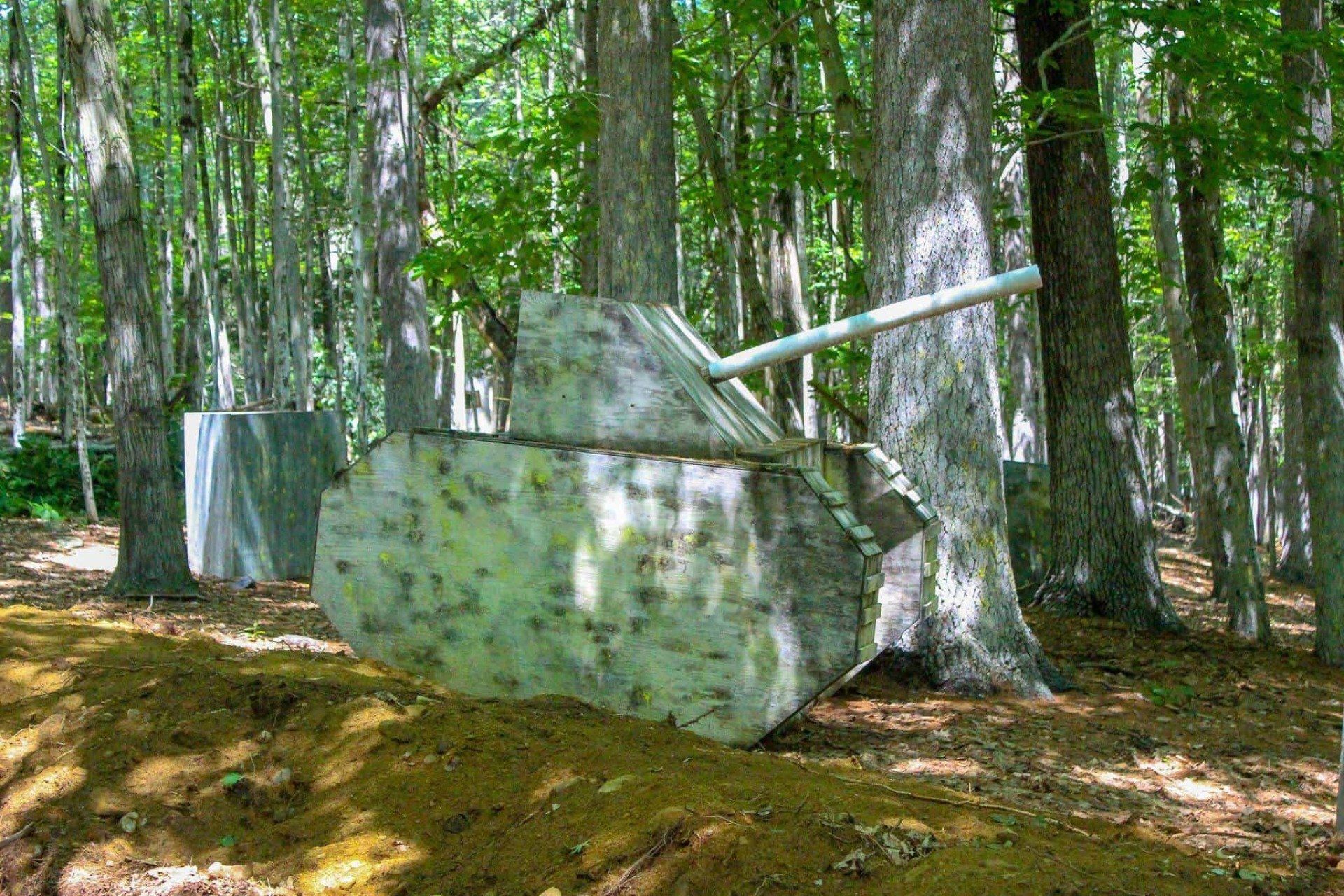 Paintball field: Stone tank and barriers in a wooded area, with trees and dirt ground.