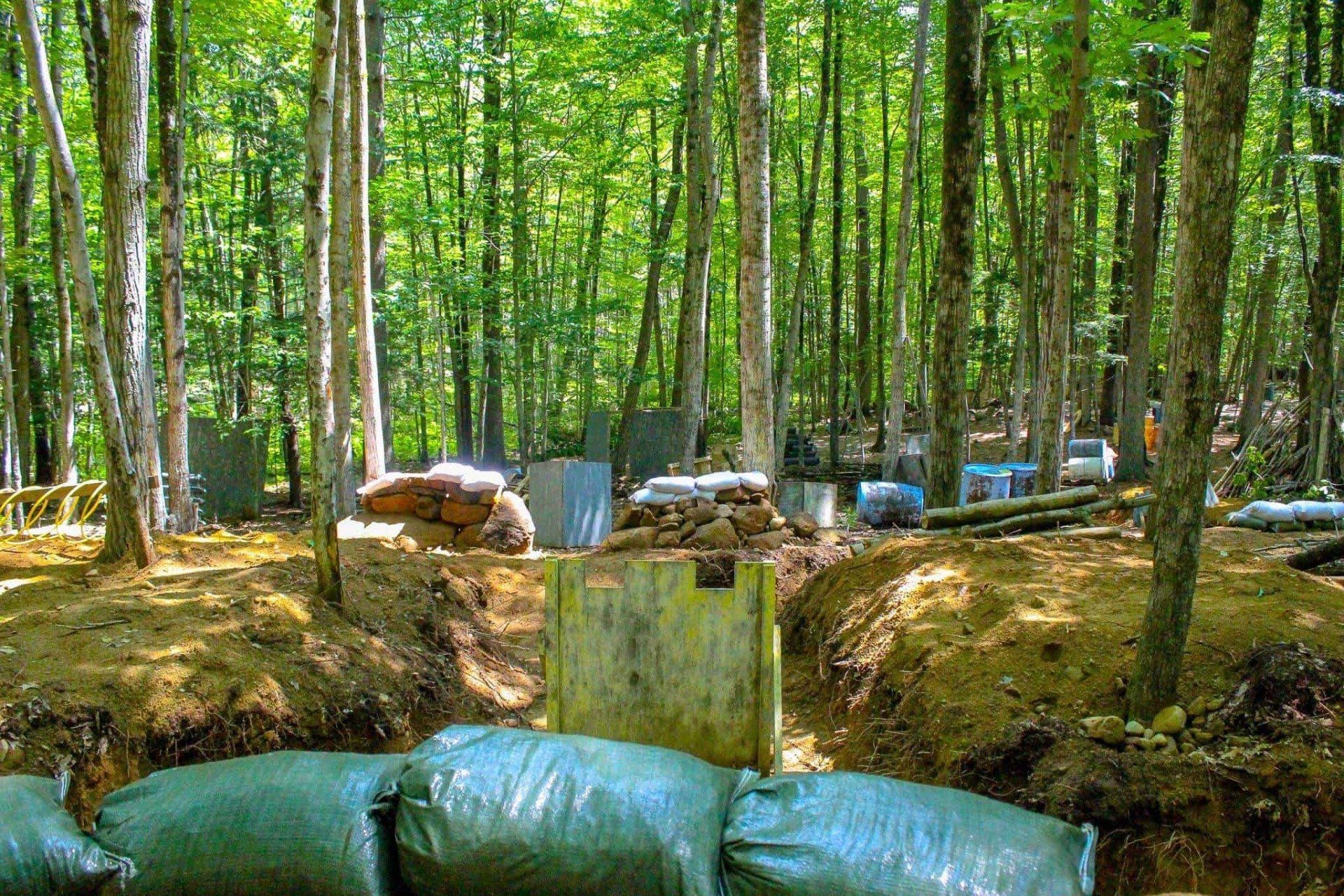 Paintball field in a forest with bunkers made of sandbags, wood, and corrugated metal.