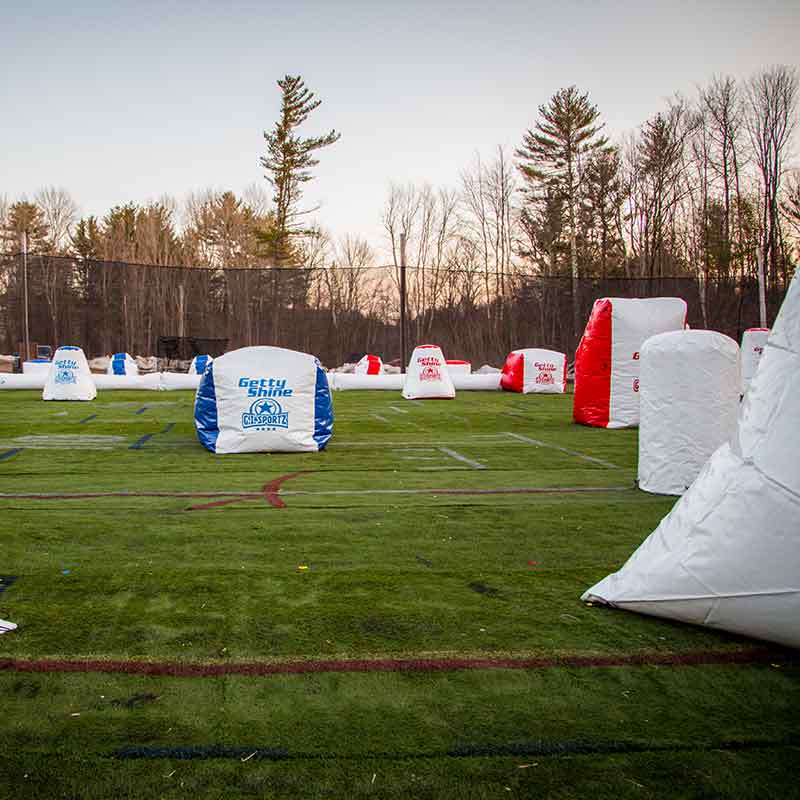 Paintball field with inflatable bunkers on green turf; trees in the background.