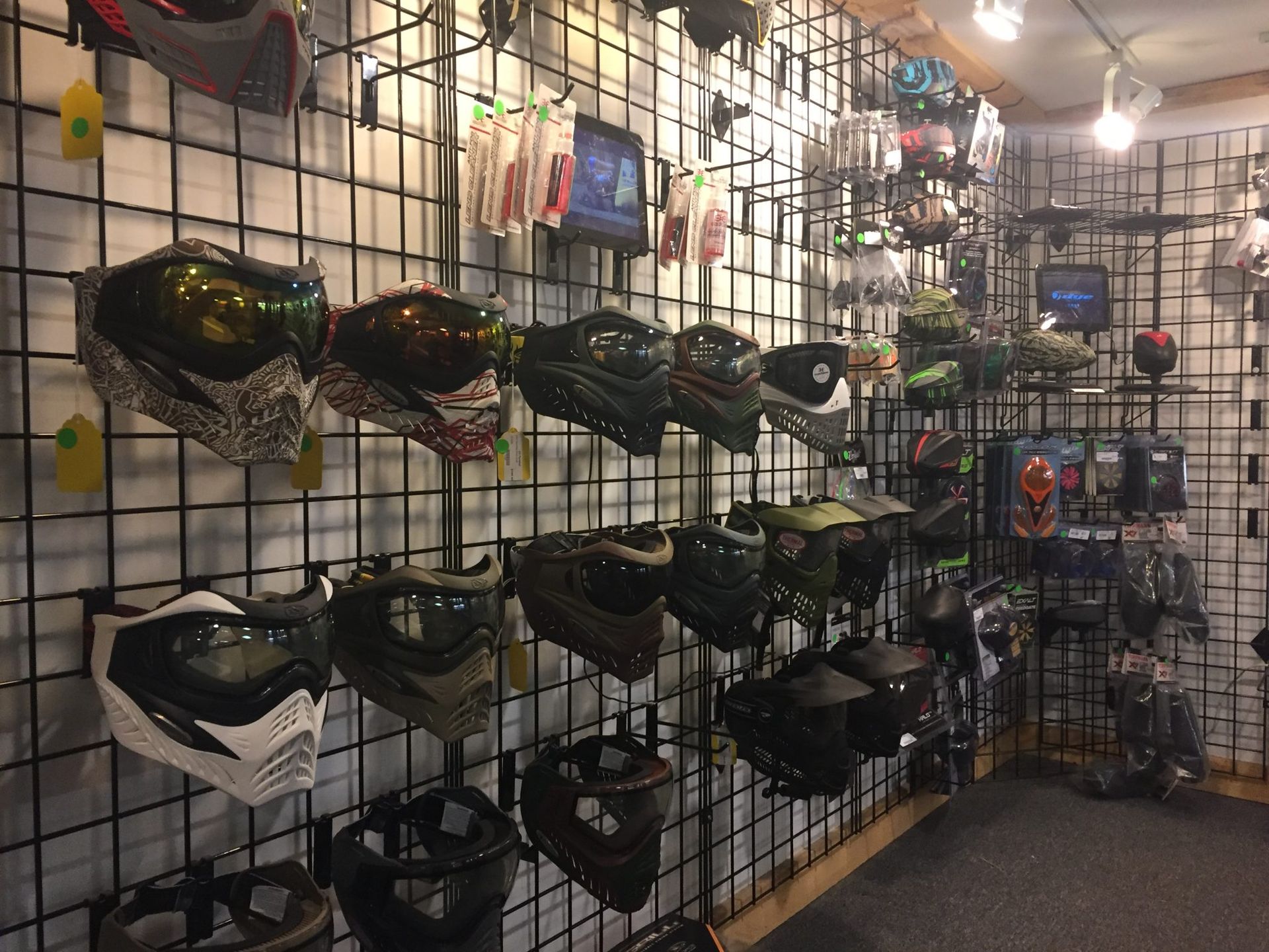Paintball masks displayed on a black grid wall in a store.