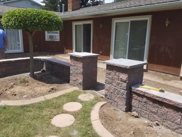 Backyard with brick columns, low walls, stone pathway, and a trimmed tree.