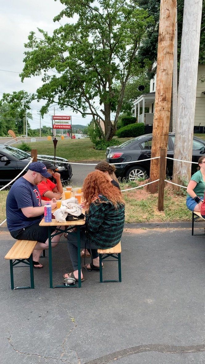 People sitting at an outdoor table; dining. Cars parked nearby.