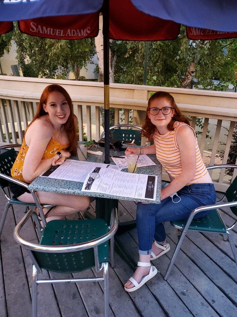 Two young women seated at a patio table, under a Samuel Adams umbrella.