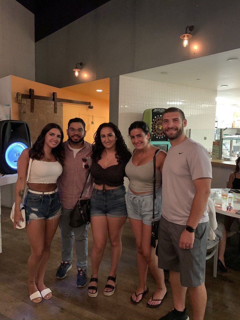 Five people smiling, posing for a photo inside a restaurant. The interior is modern with wood accents and a light color scheme.