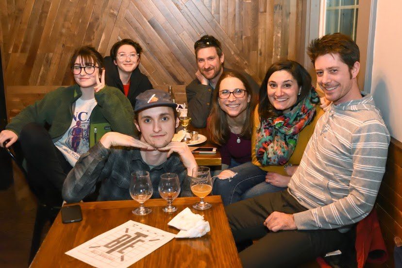 Group of people smiling at a table with drinks in a warmly lit room.
