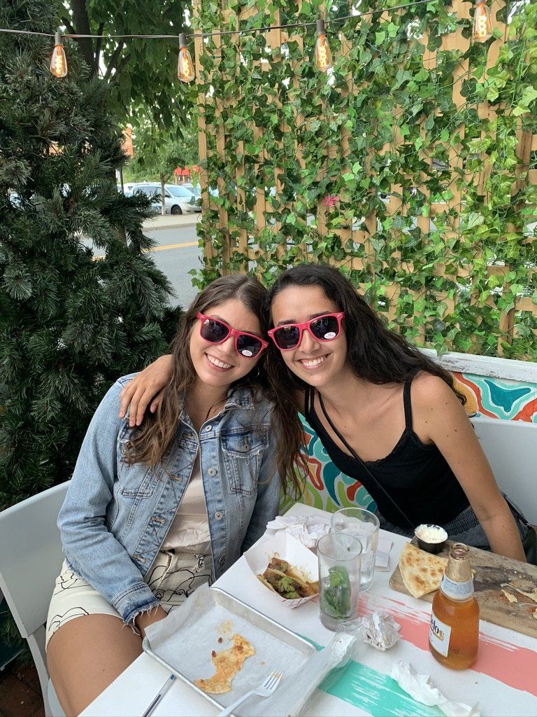 Two smiling people with red sunglasses outdoors, sitting at a table.