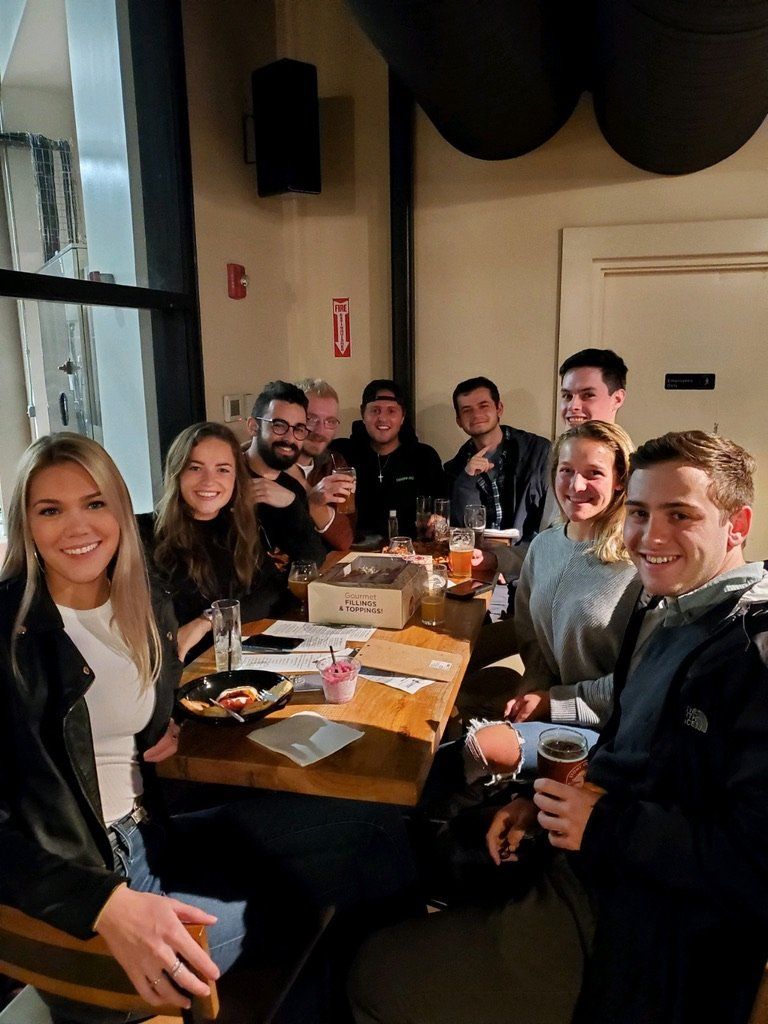 Group of people at a table in a bar, smiling and looking at the camera, holding drinks.