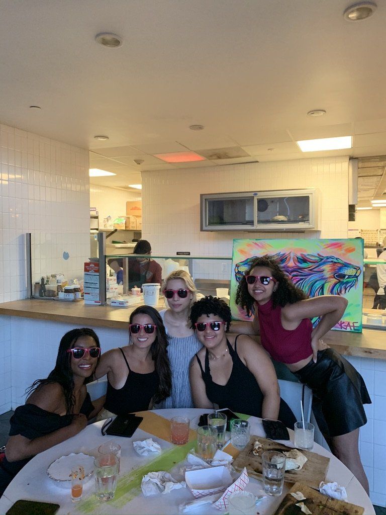 Five people wearing sunglasses pose at a table. Messy table, restaurant interior.